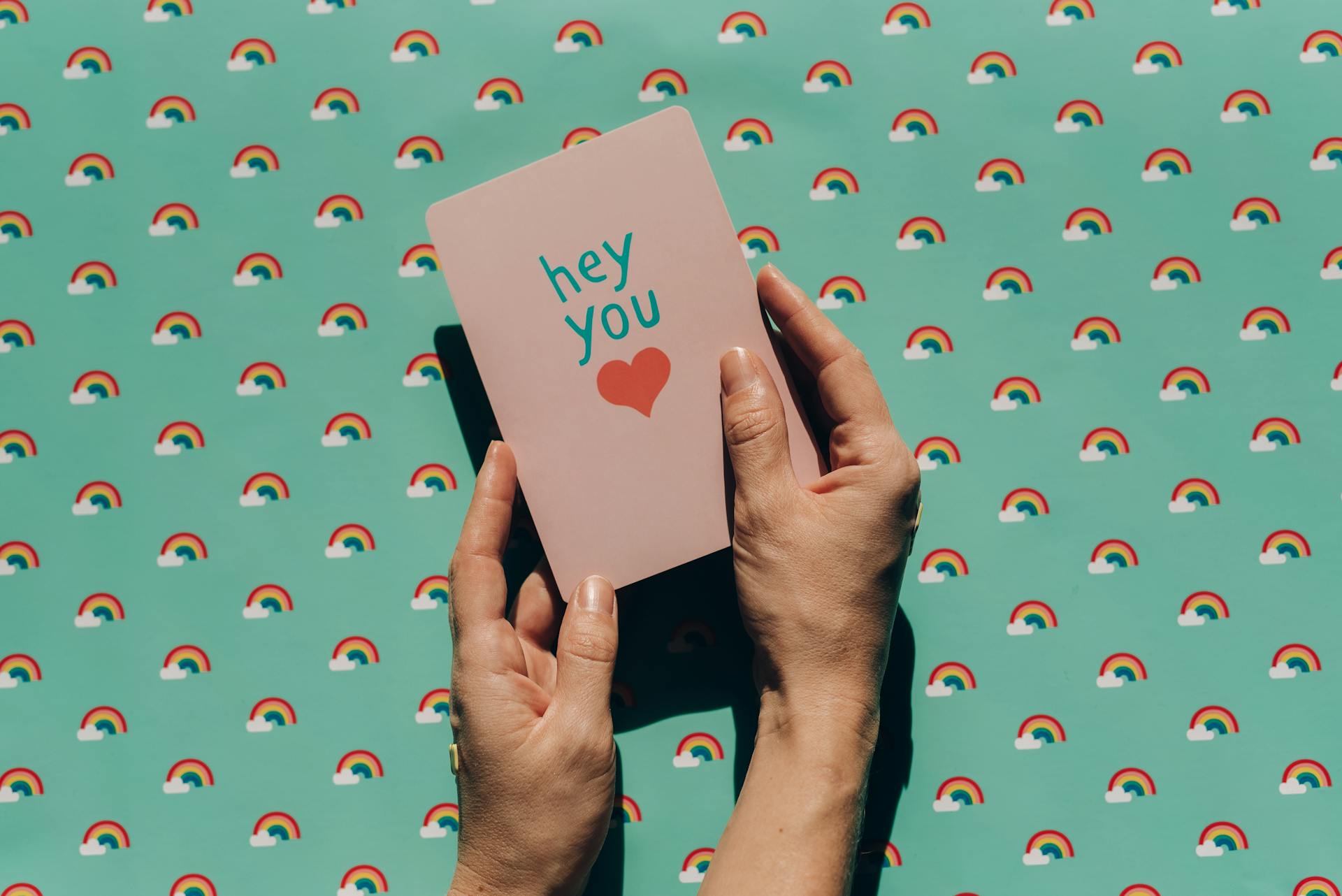 Card with 'hey you' text and heart on a rainbow patterned background creating a cheerful vibe.