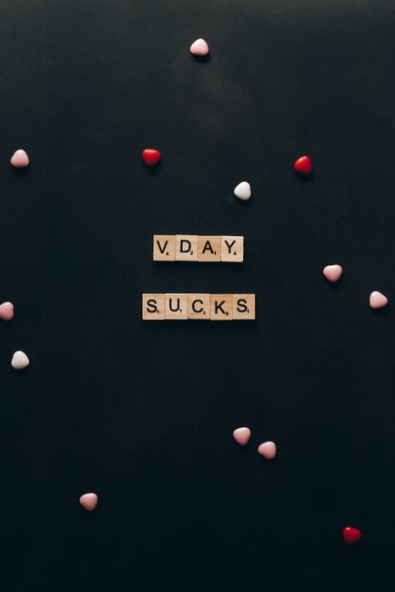 Fotomural Las fichas de Scrabble forman 'V DAY SUCKS' sobre un fondo oscuro con decoraciones en forma de corazón dispersas.