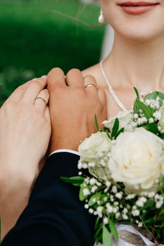 Close-up of a couple's hands with rings and a bride holding a bouquet, symbolizing love.