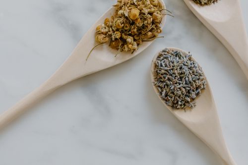 Free Close-up of chamomile and lavender dried herbs in wooden spoons on white marble. Stock Photo