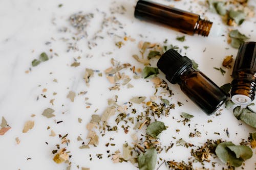 Close-Up Shot of Essential Oil Bottles and Herbs on White Surface