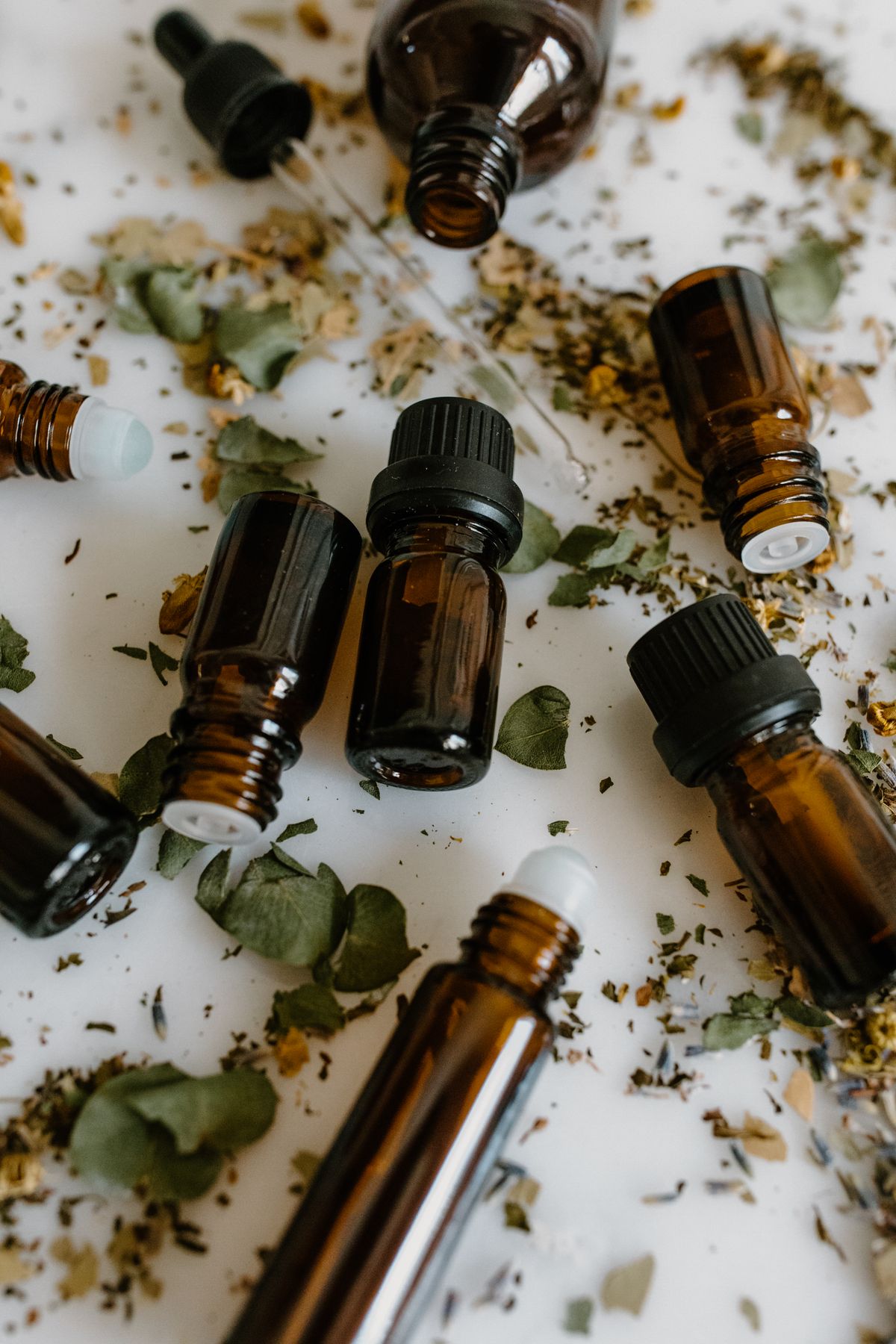 Brown glass essential oil bottles arranged with dried herbs on a white surface