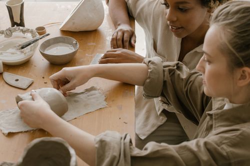 Free Two women engaging in pottery crafting with clay and tools on a tabletop. Stock Photo