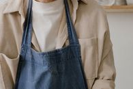 A close-up view of a person wearing a denim apron over a beige shirt.