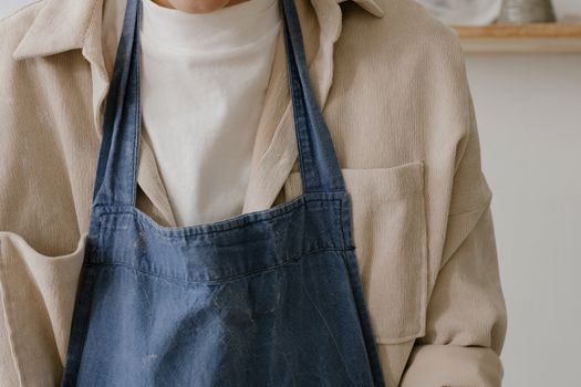 A close-up view of a person wearing a denim apron over a beige shirt.