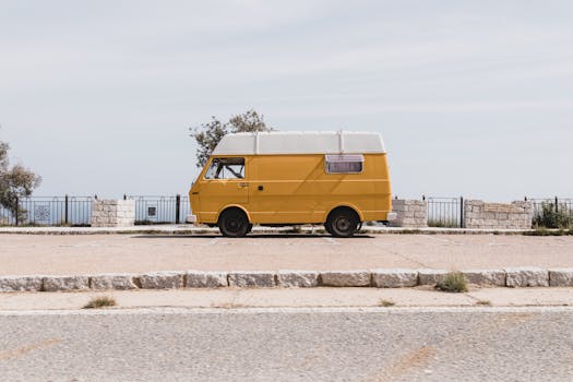 A classic yellow van parked by a scenic seaside road in Sardinia, Italy, under a clear sky.