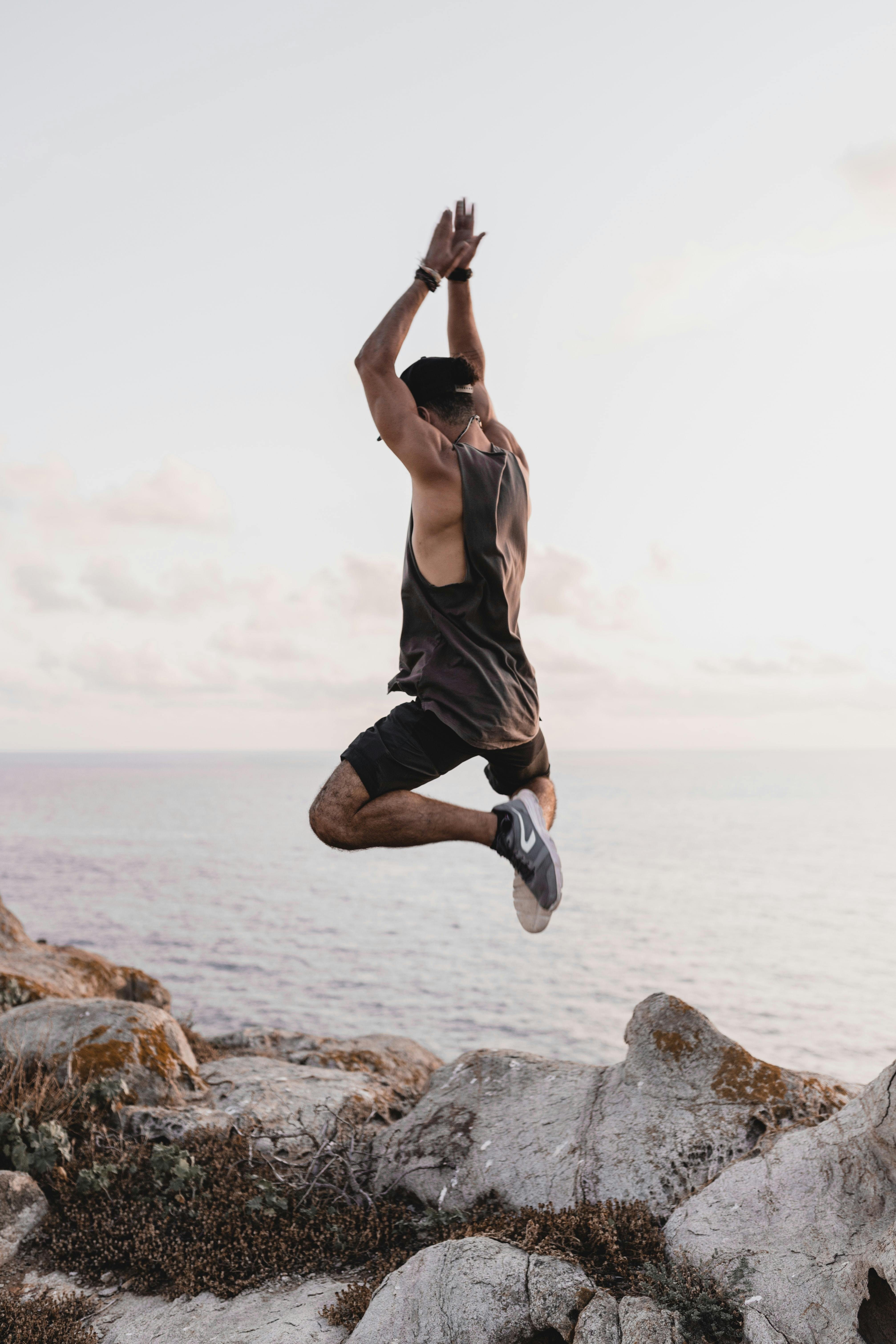 Energetic man leaping on rocks by the sea in Sardinia, Italy at sunset.