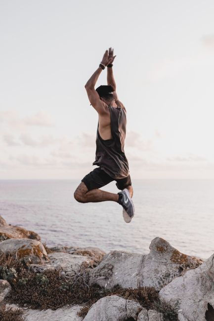 Energetic man leaping on rocks by the sea in Sardinia, Italy at sunset.