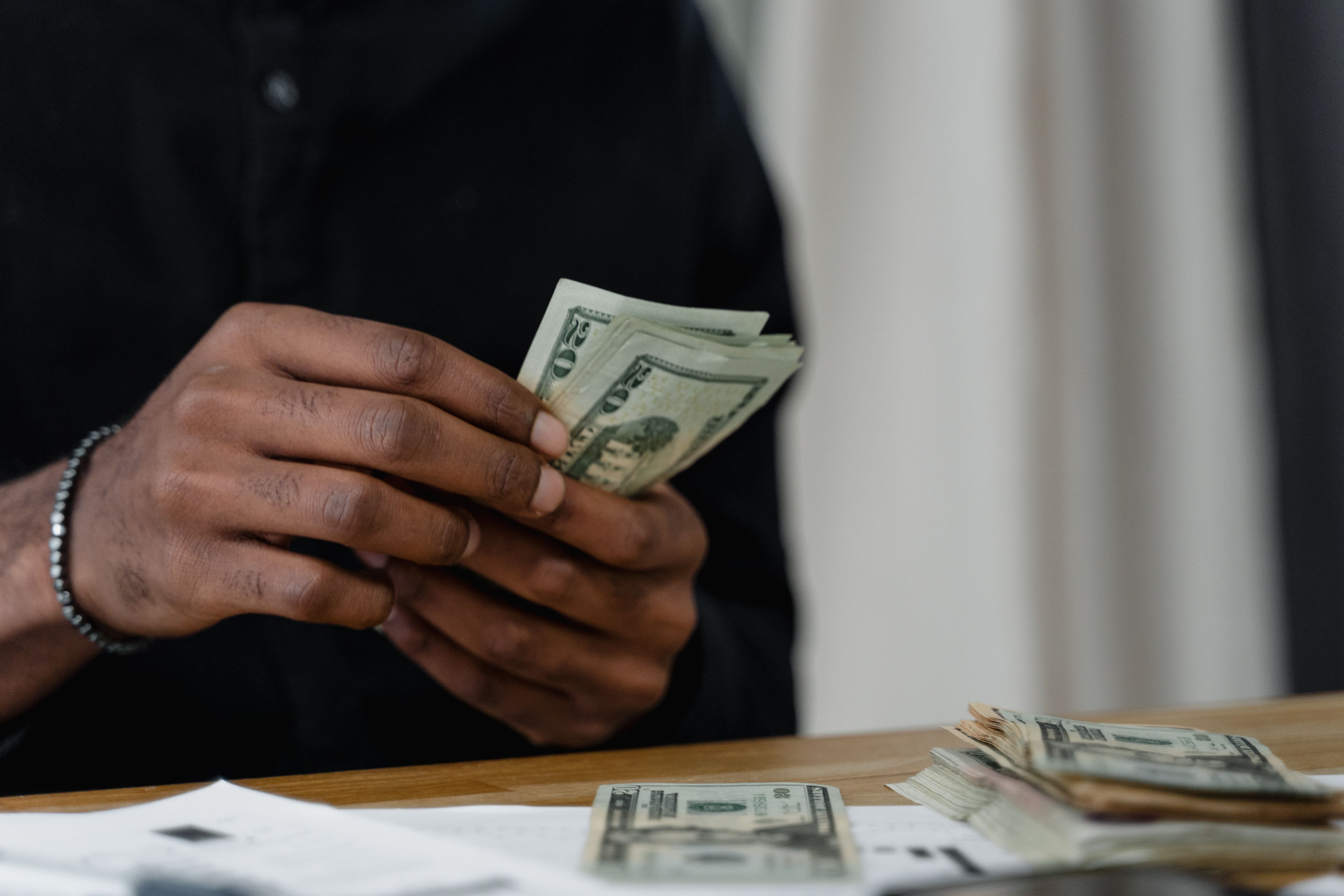 Person counting cash at a desk while reviewing financial paperwork