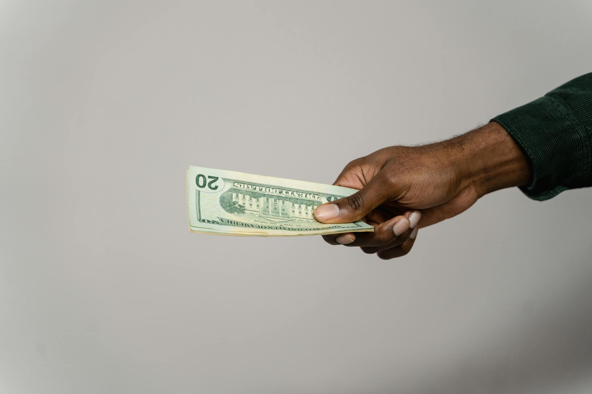 A hand holding a twenty dollar bill against a plain gray background.