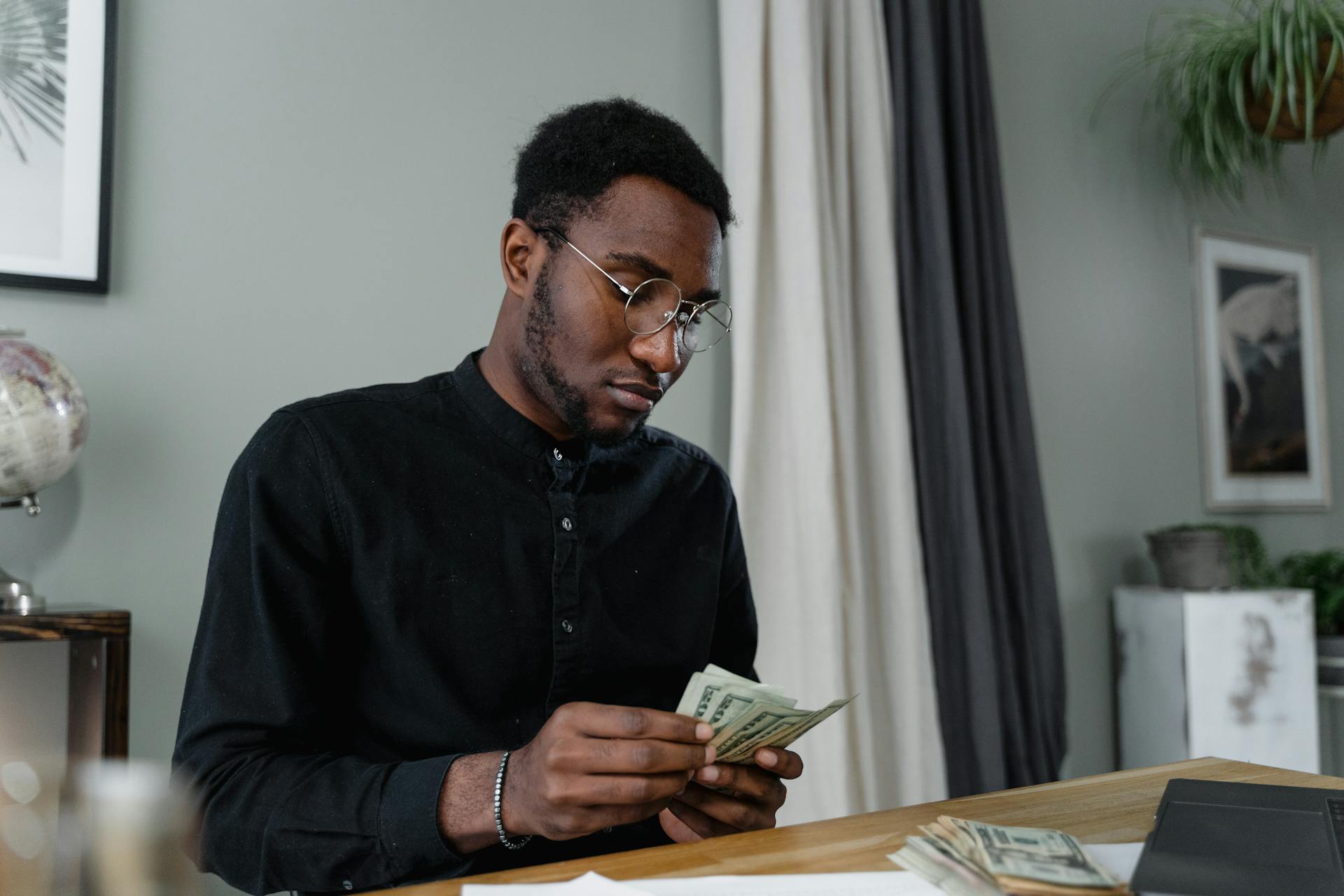 A focused man in glasses counting cash at a desk, indicating financial management.