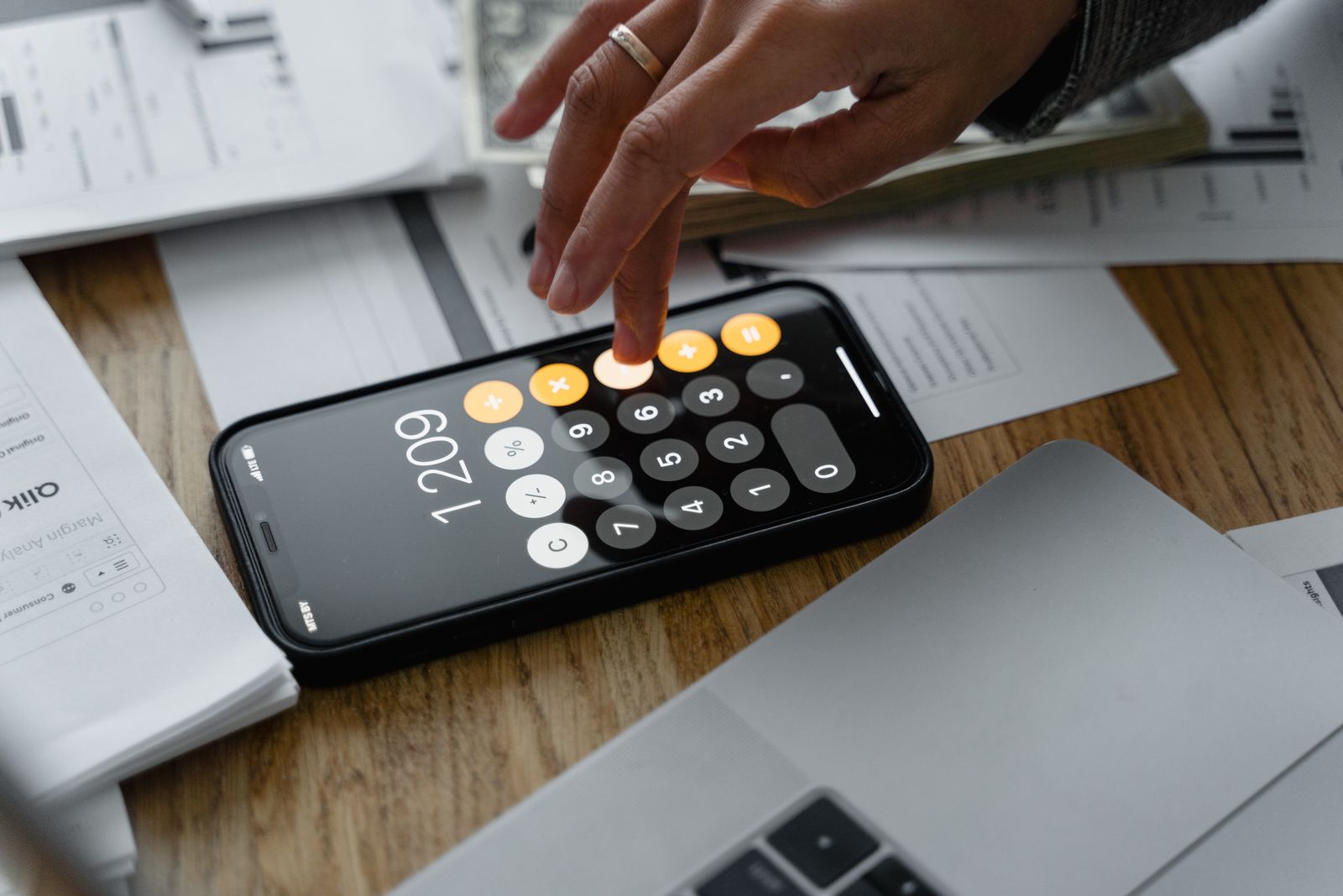 Free Close-up of a person using a smartphone calculator on a table with documents for financial calculations. Stock Photo