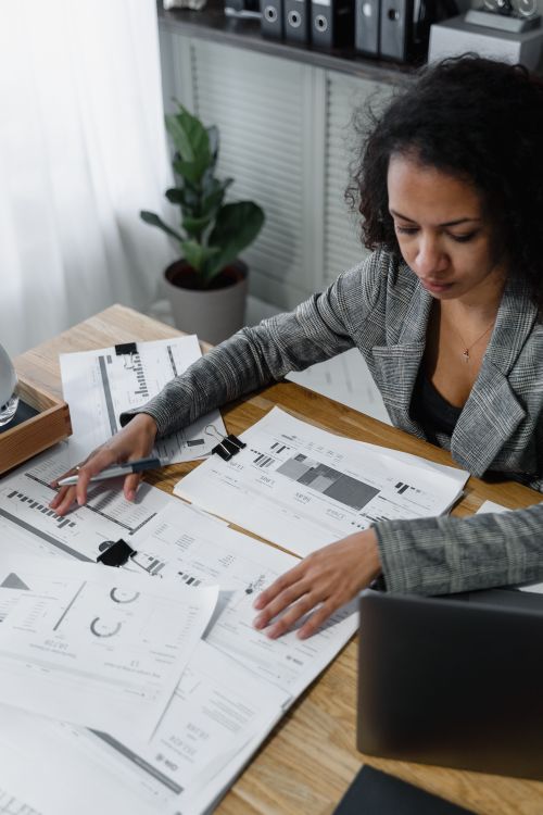 Free Professional woman reviewing documents and charts at a desk in a modern office. Stock Photo