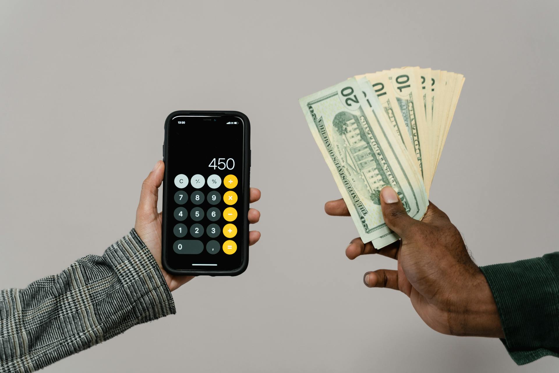 Two hands displaying cash and a smartphone calculator with a digital display, indicating a financial transaction.