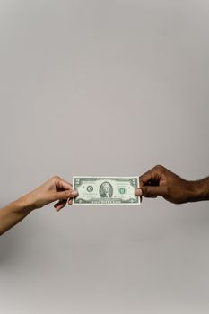 A dollar bill is exchanged between two diverse hands on a neutral background.