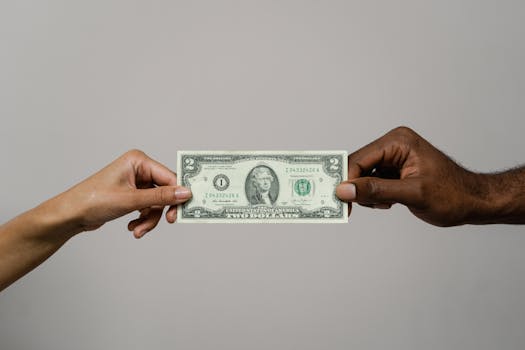Two hands exchanging a two dollar bill, symbolizing financial transaction.