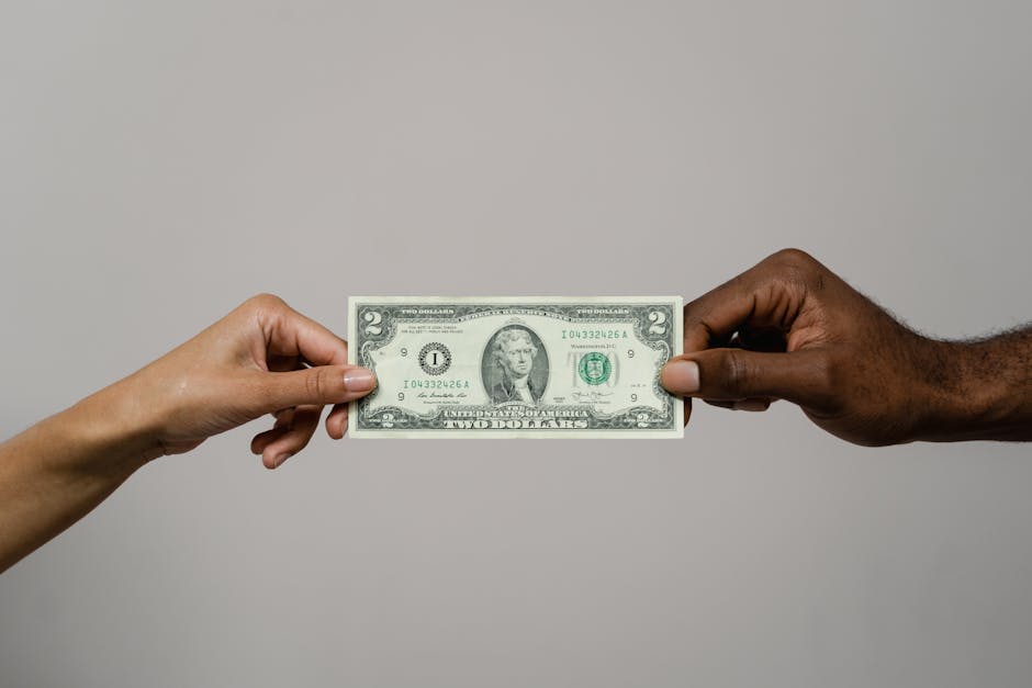 Two hands exchanging a two dollar bill, symbolizing financial transaction.