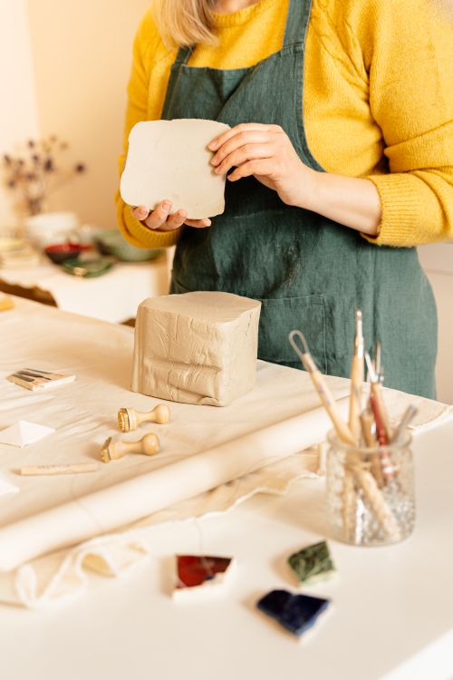 Free An artisan shapes clay in a pottery studio, using tools and wearing a yellow sweater. Stock Photo