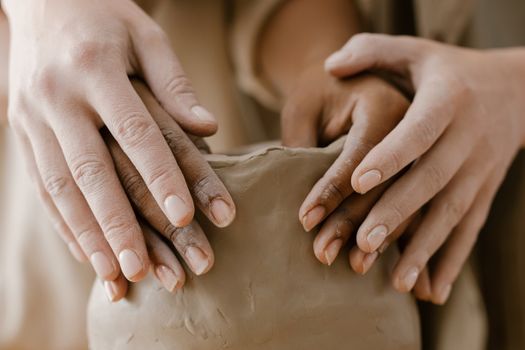 Close-up of diverse hands sculpting clay, symbolizing unity in pottery making.
