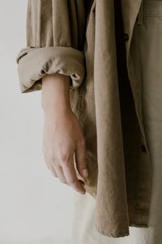 Artistic close-up of a hand in a beige long sleeve shirt on a neutral background.