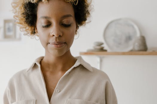 Calm portrait of an African American woman with curly hair and a beige shirt indoors.