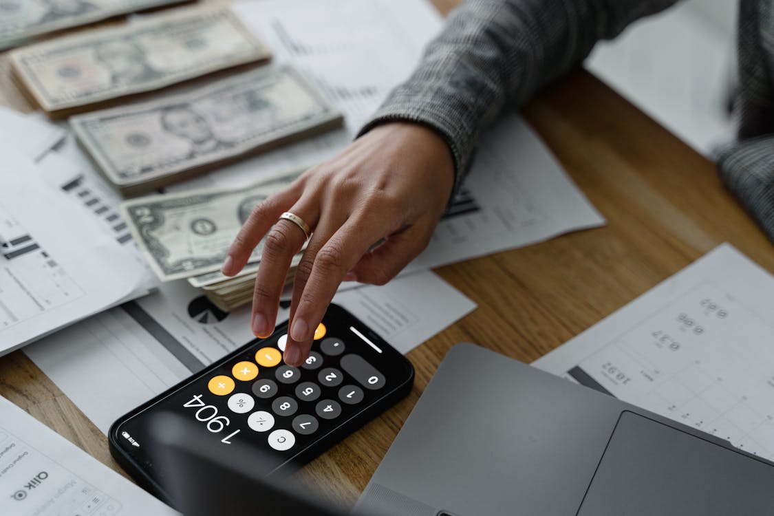 Free Hand of a Person Using a Calculator Near Cash Money on Wooden Table Stock Photo