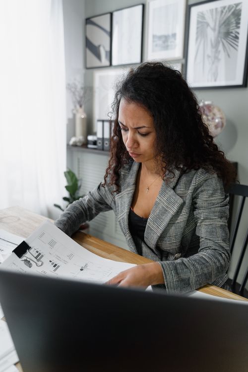 Free Businesswoman reviewing financial documents at office desk, showcasing concentration and professionalism. Stock Photo