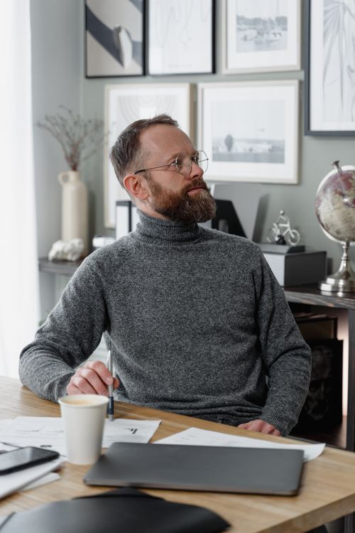 Free Bearded businessman in glasses seated at desk with coffee in modern office. Stock Photo
