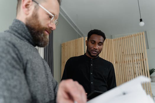 Two men discussing documents in a modern office setting.