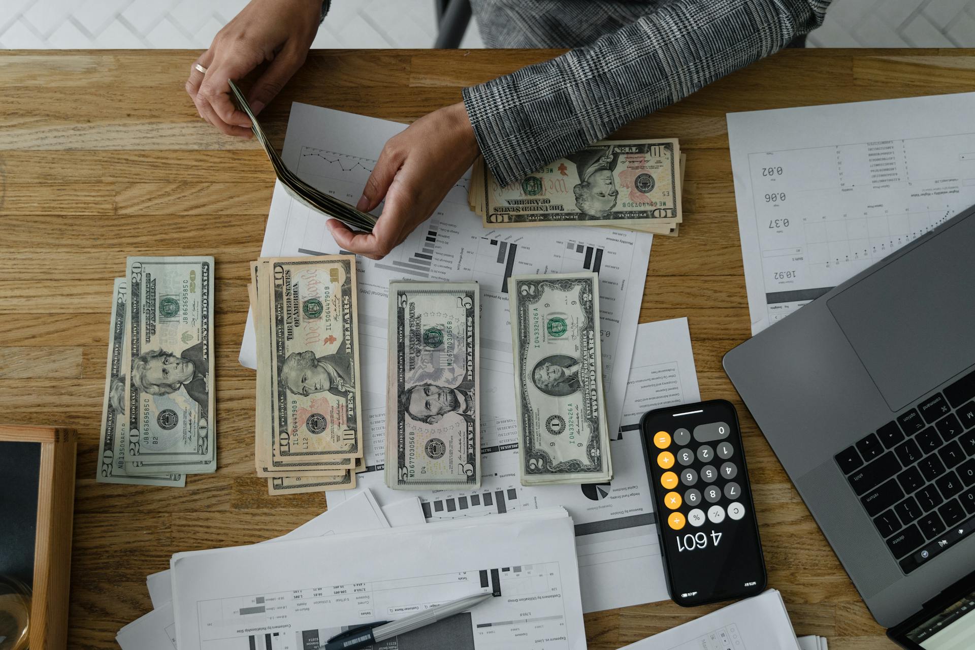 A Person Arranging Cash Money on Wooden Table