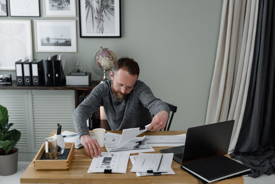 Professional reviewing documents at an office desk with a laptop and coffee.