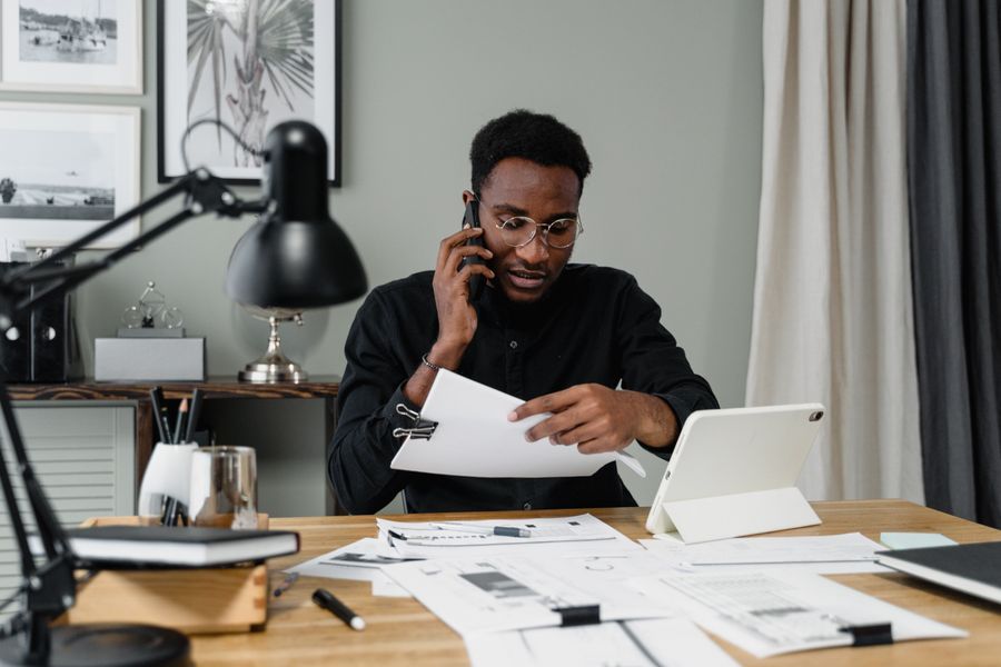 A bursar in black reviewing school fee documents on the phone in a modern office