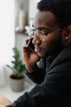 Close-up of a man wearing glasses, making a phone call indoors with a focused expression.