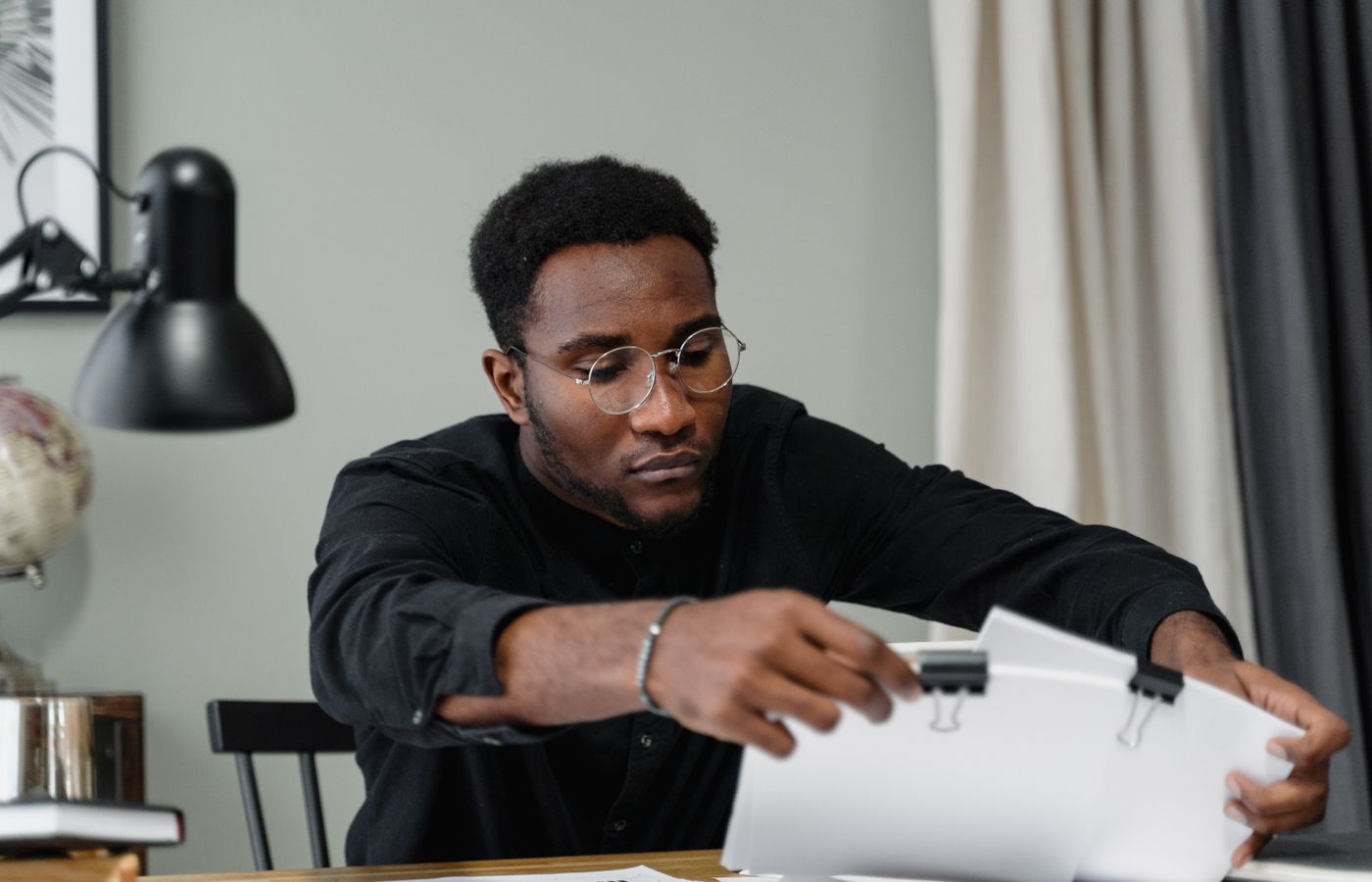 Professional man with glasses reviews documents at a desk in an office setting, emphasizing concentration.