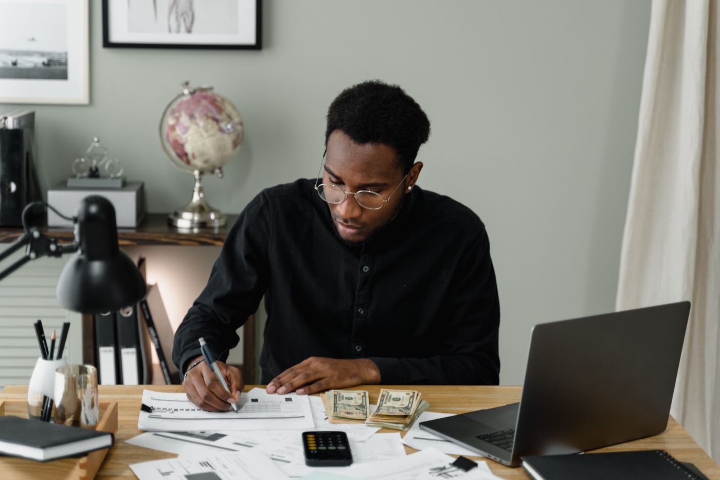 Black man using a calculator and laptop to plan a longer-term personal budget