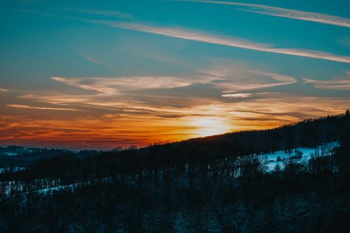 Free Breathtaking winter sunset over snowy woodland and hills with vibrant sky colors. Stock Photo