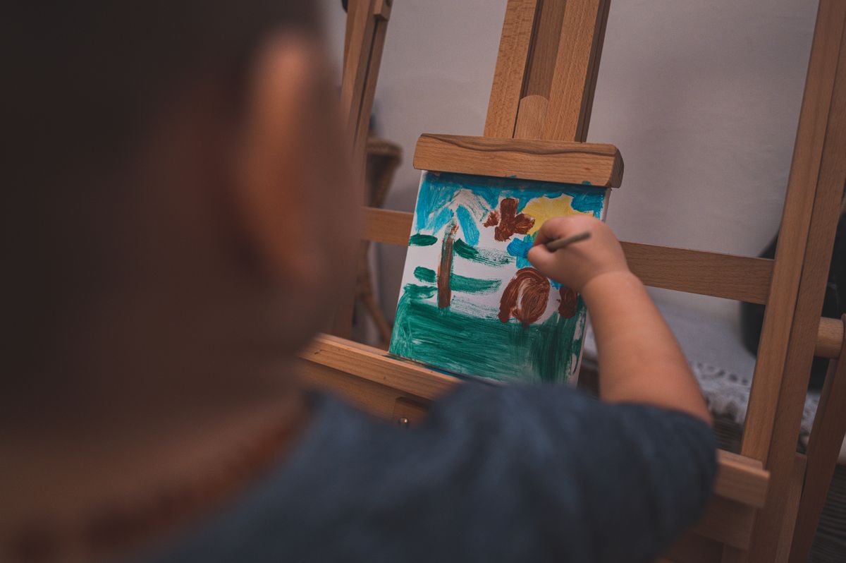 Young child painting a colorful picture on a canvas at an easel indoors