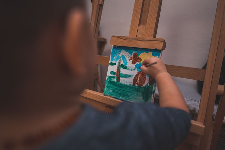 A young child painting a colourful picture on a canvas at an easel — photo by Jan Kořiva on Pexels