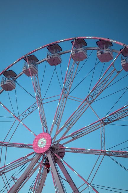 Low angle view of a vibrant Ferris wheel at an amusement park under a clear blue sky.