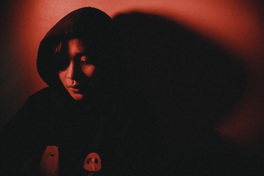 Artistic portrait of a person in a hood, illuminated by red light creating dramatic shadows.