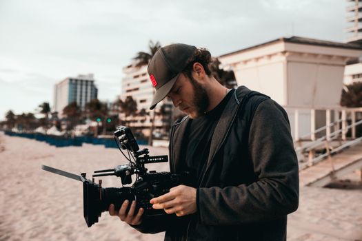 A filmmaker adjusts camera gear on a sandy beach, preparing for a shoot.