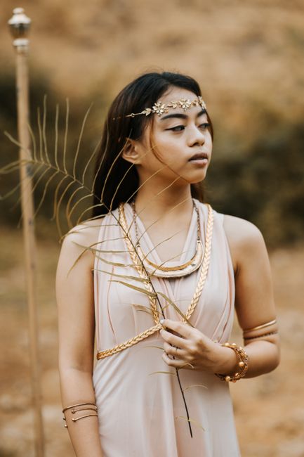A young woman in goddess-inspired attire with golden accessories and holding a Reed.