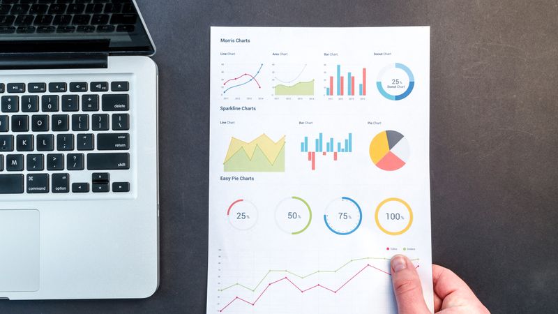 Detailed charts and graphs on a document next to a laptop, representing data analysis.