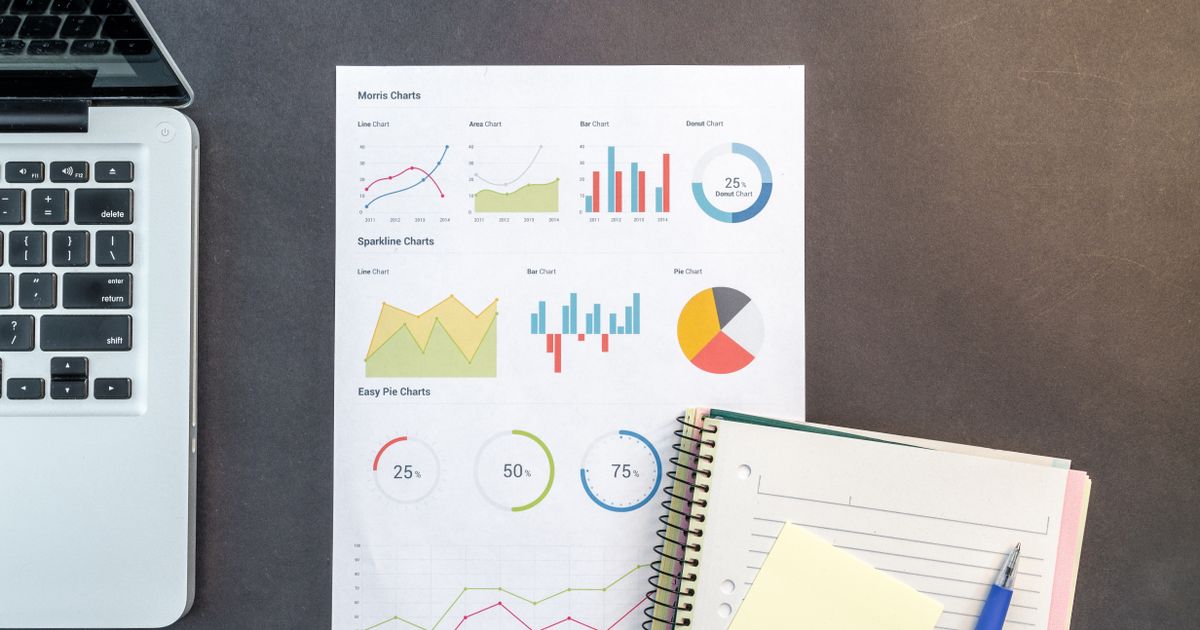 Top-down view of a desk with charts, a laptop, and notebooks, ideal for data analysis themes.