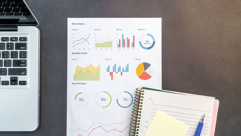 Top-down view of a desk with charts, a laptop, and notebooks, ideal for data analysis themes.