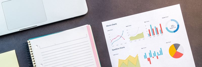 Top view of a laptop, notebook, and data charts on a table, ideal for business and work themes.