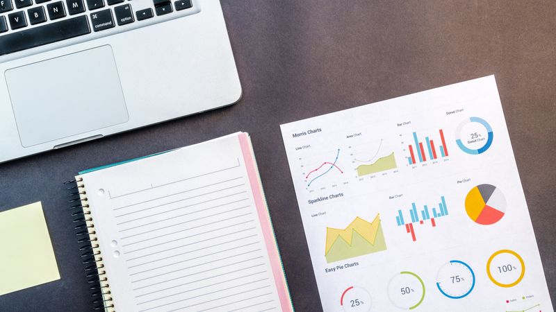 Top view of a laptop, notebook, and data charts on a table, ideal for business and work themes.