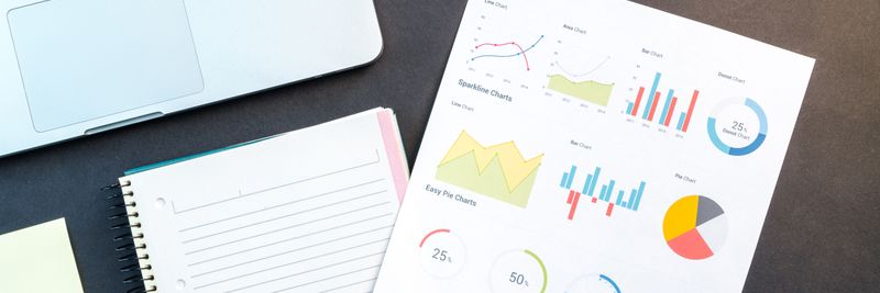 Flatlay of business report with colorful charts, a notebook, and a laptop for data analysis on a desk.