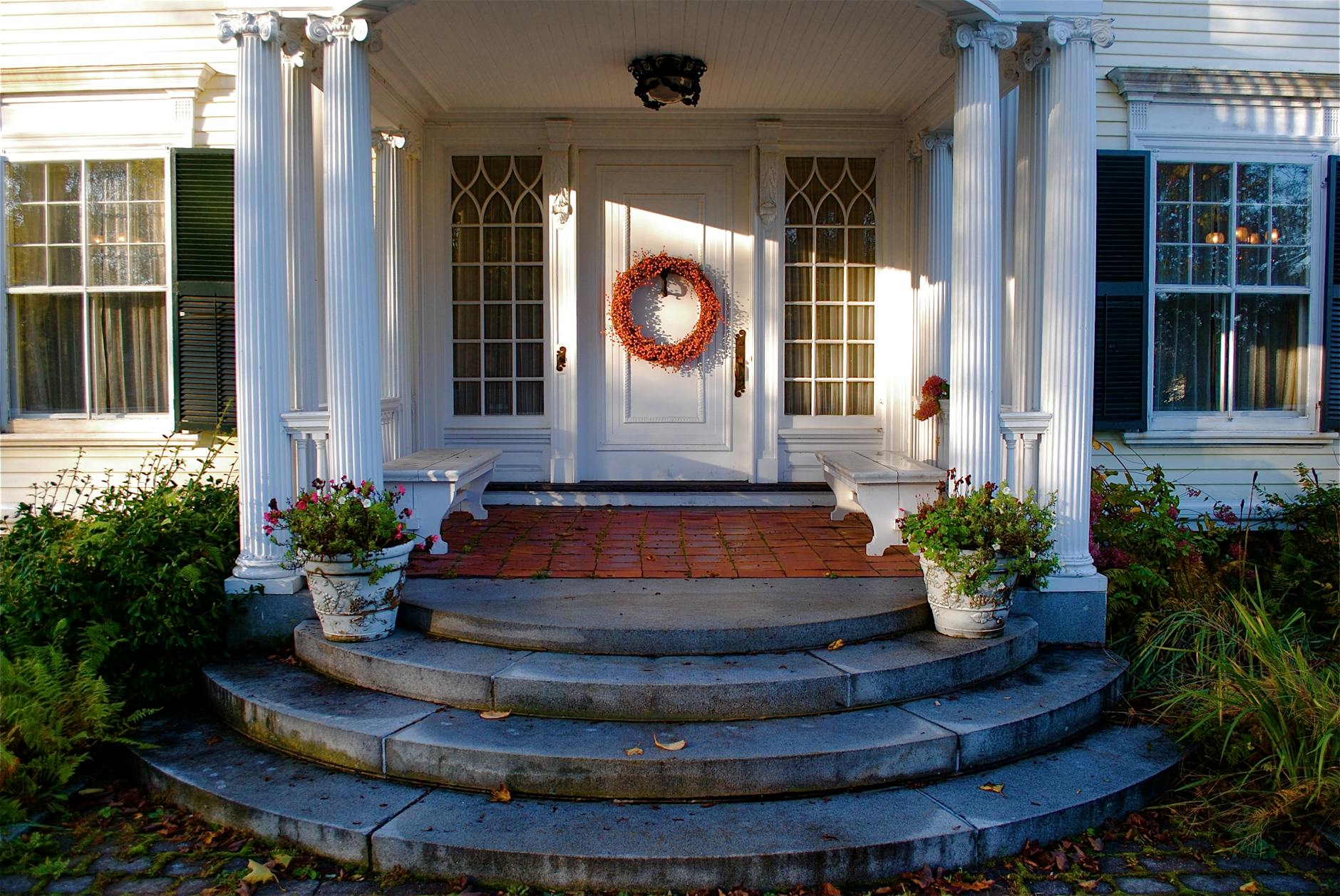 Charming entrance porch with white pillars, autumn wreath, and curved stone steps in Bath, Maine.