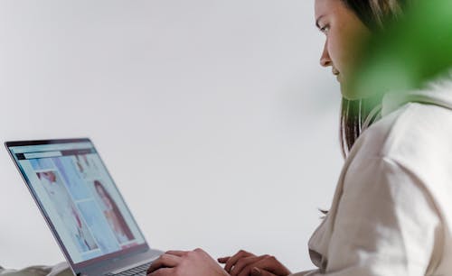 Side view of focused female freelancer typing on modern netbook while working remotely near white wall and green leaf at home